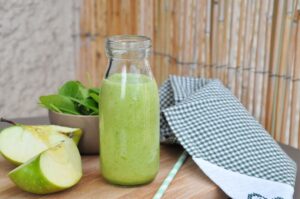 Sour apple smoothie in a glass bottle placed on a wodden board having surroundings of apples