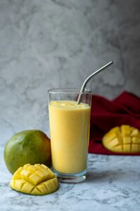 Mango pineapple smoothie in a glass with mango as a decorative piece on side