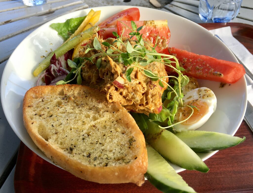 Tuna salad with eggs and bread placed in a white plate on top of a table